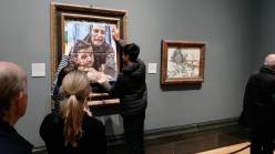 Two people pasting an image of a crying mother and child over a painting in a gallery.