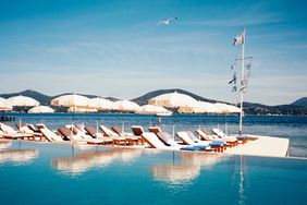 A pool by the sea, surrounded by white deck chairs and umbrellas